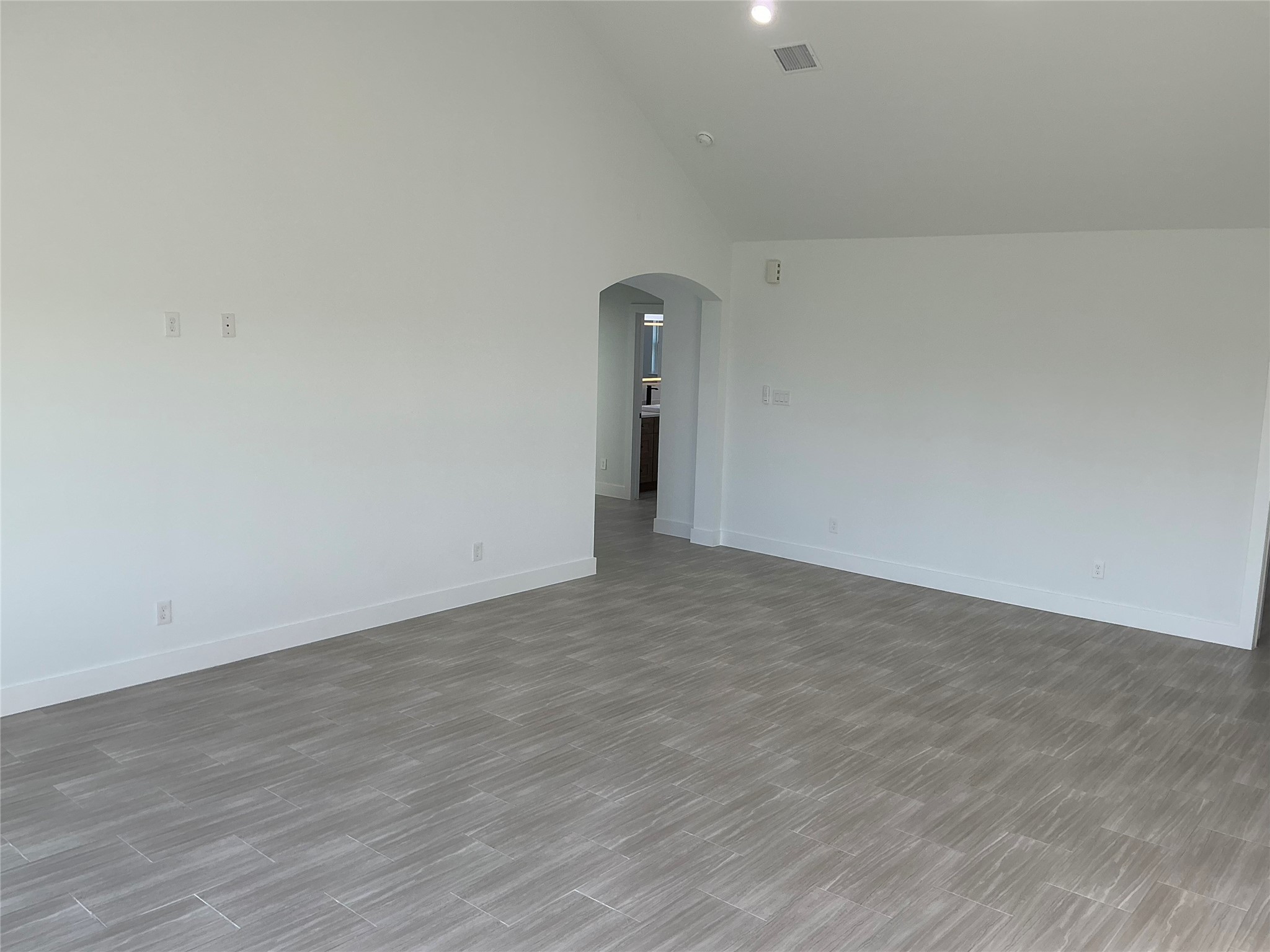 471 Buffalo Trail Angleton, TX 77515 - Photo 7 of 35 This photo features a spacious room with light gray tile flooring and white walls, offering a clean, modern look. The arched doorway leads to another area, enhancing the open layout.