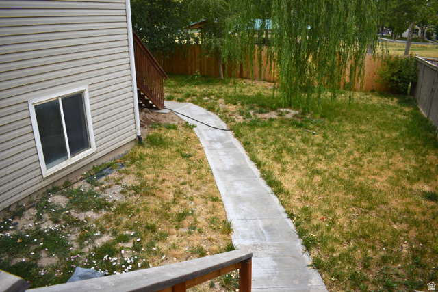 3327 East Windhover Road Eagle Mountain, UT 84005 - Photo 38 of 38 Expansive backyard with a curved concrete pathway, featuring a mature weeping willow tree and wood privacy fencing