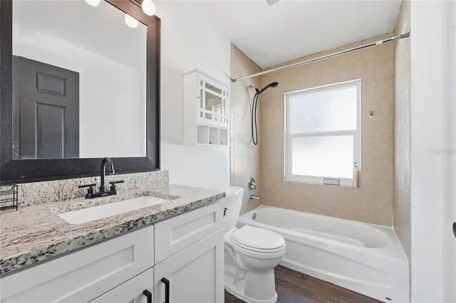 a bathroom with a granite countertop sink toilet vanity mirror next to a window
