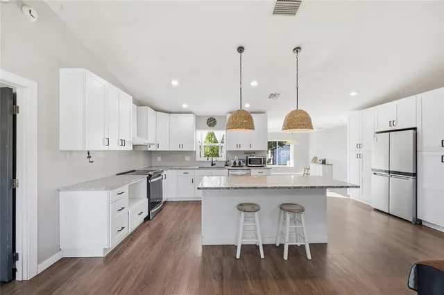 a kitchen with stainless steel appliances granite countertop a island a stove a refrigerator and white cabinets with wooden floors