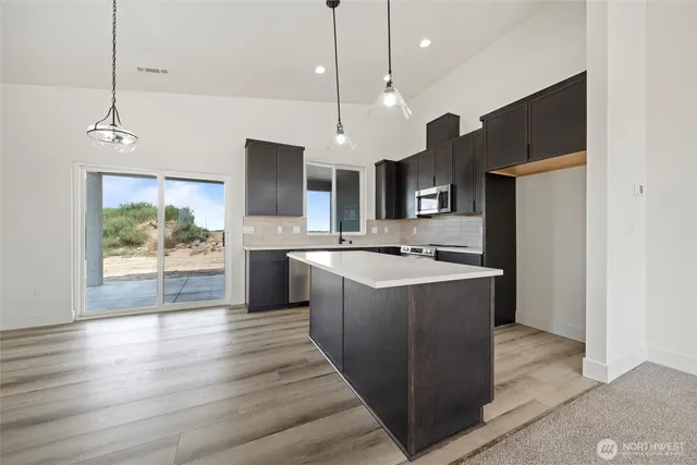 a large kitchen with stainless steel appliances kitchen island a large counter top a sink a refrigerator and a wooden floor