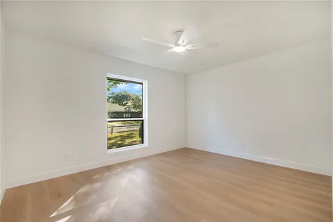 an empty room with wooden floor chandelier fan and windows