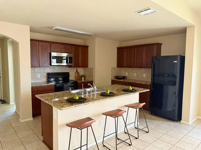 a kitchen with kitchen island granite countertop a table chairs microwave and refrigerator