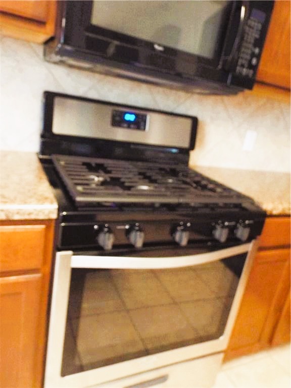 3609 Eagle Fledge Terrace Pflugerville, TX 78660 - Photo 11 of 15 Kitchen with black microwave, gas stove, wood finish cabinets.