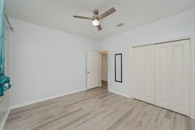 an empty room with wooden floor chandelier fan and windows