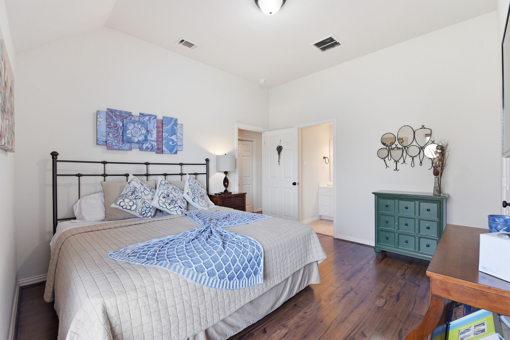 223 South Bauer Point Circle Spring, TX 77389 - Photo 30 of 50 This cozy bedroom features a vaulted ceiling and hardwood floors. It includes a stylish iron bed with decorative bedding, a green dresser, and wall art. A door leads to an ensuite bathroom, enhancing functionality and privacy.