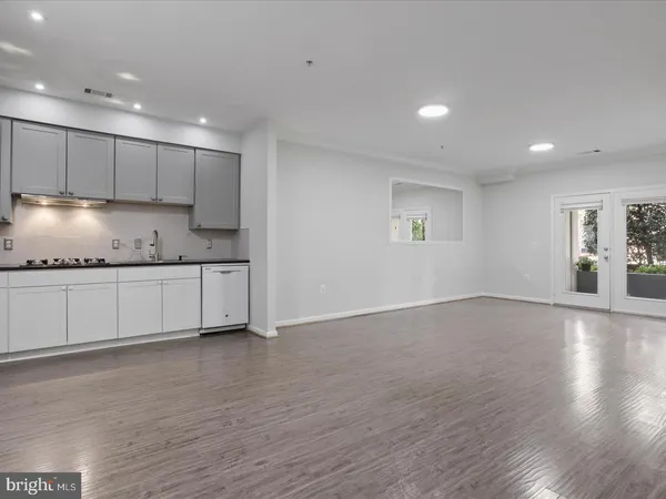 a view of an empty room with wooden floor and kitchen