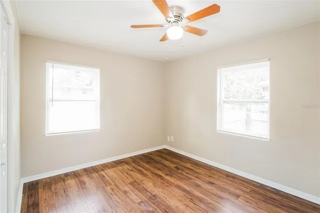 an empty room with wooden floor ceiling fan and windows