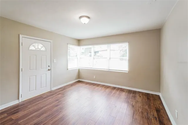 a view of an empty room with wooden floor and a window