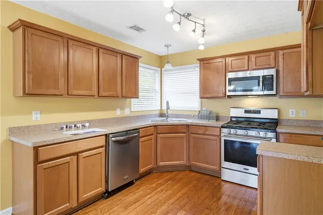 a kitchen with stainless steel appliances granite countertop hardwood floor sink stove and wooden cabinets