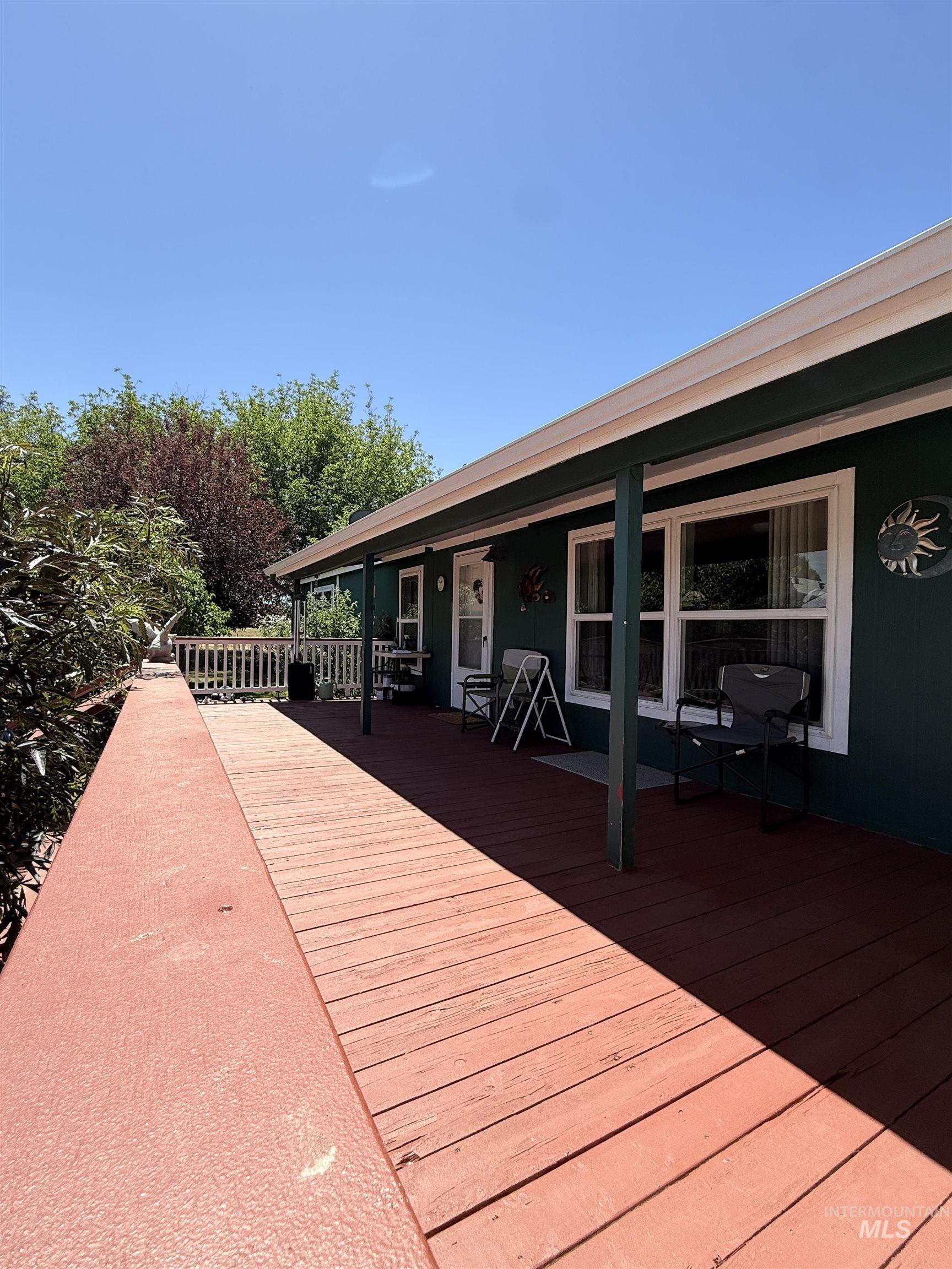 2750 Alden Road, Unit 12 12 Fruitland, ID 83619 - Photo 7 of 38 Expansive front porch with red-toned wood decking, dark green siding, white trim, multiple windows, and a white entry door