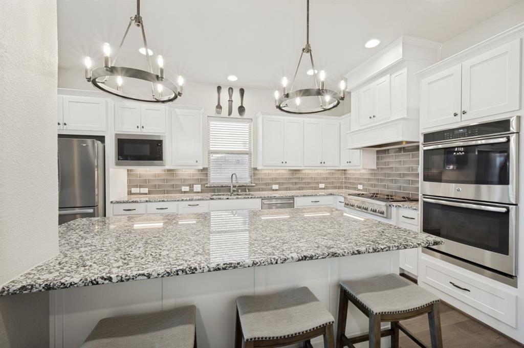 2721 Old Shire Path Road Prosper, TX 75078 - Photo 5 of 39 Kitchen featuring a large island with stone countertop, white shaker cabinetry, stainless steel appliances, and a subway tile backsplash