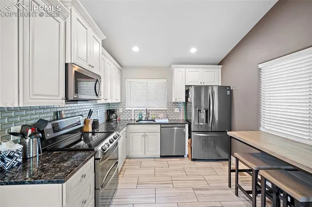 a kitchen with stainless steel appliances granite countertop a refrigerator a stove a sink a dining table and chairs