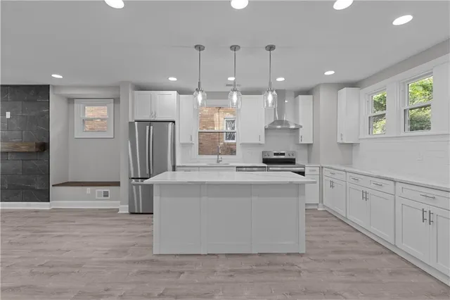 a kitchen with stainless steel appliances granite countertop a stove a sink a refrigerator and white cabinets with wooden floor