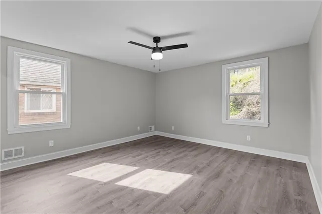 an empty room with wooden floor chandelier fan and windows