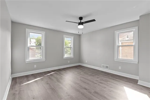 a view of an empty room and window a ceiling fan and wooden floor