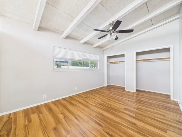 an empty room with wooden floor ceiling fan and windows
