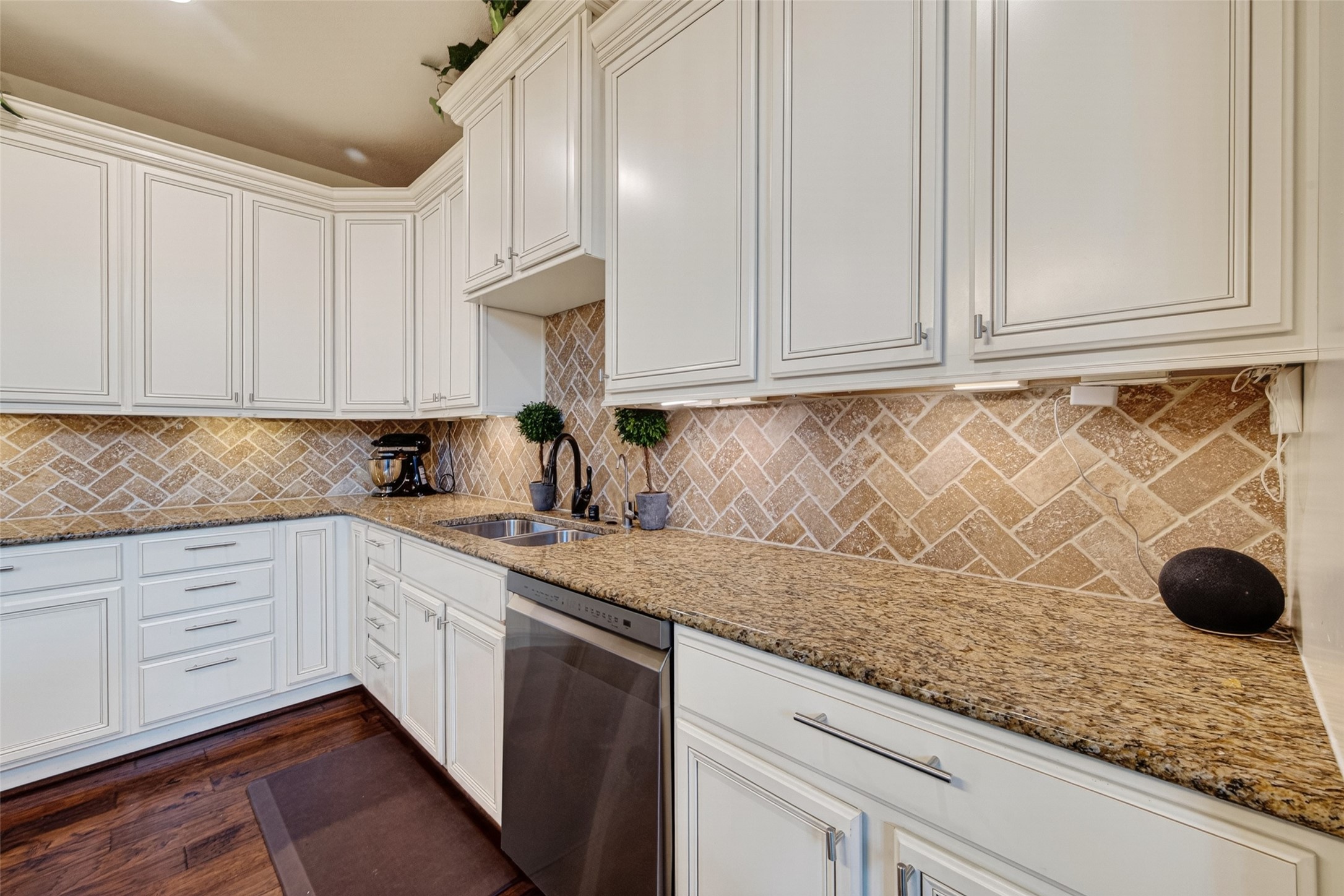 25611 Ellis Ridge Court Katy, TX 77494 - Photo 14 of 49 This kitchen features elegant white cabinetry, granite countertops, and a stylish herringbone tile backsplash. It includes a modern stainless steel dishwasher and ample storage space, creating a functional and attractive cooking area.