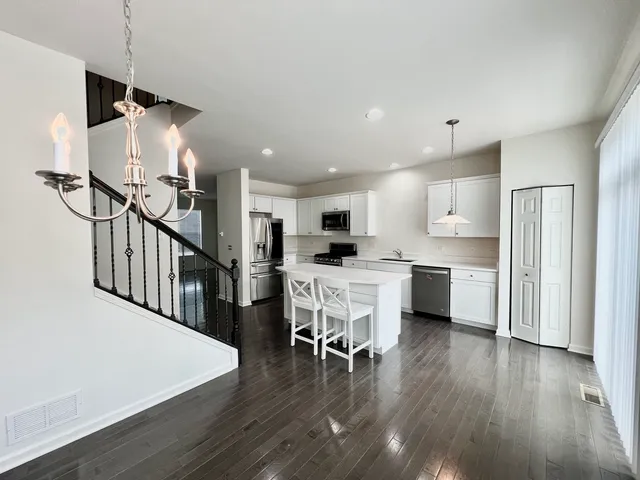 a kitchen with stainless steel appliances kitchen island a refrigerator a stove a dining table and chairs with wooden floor