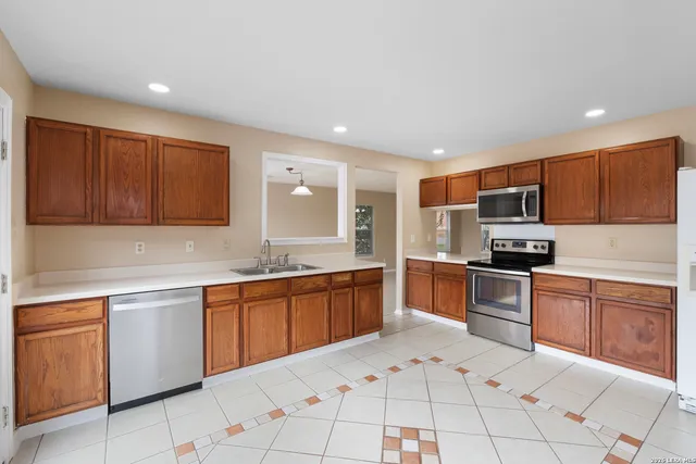 a kitchen with stainless steel appliances granite countertop a stove top oven a sink dishwasher and a refrigerator with wooden cabinets