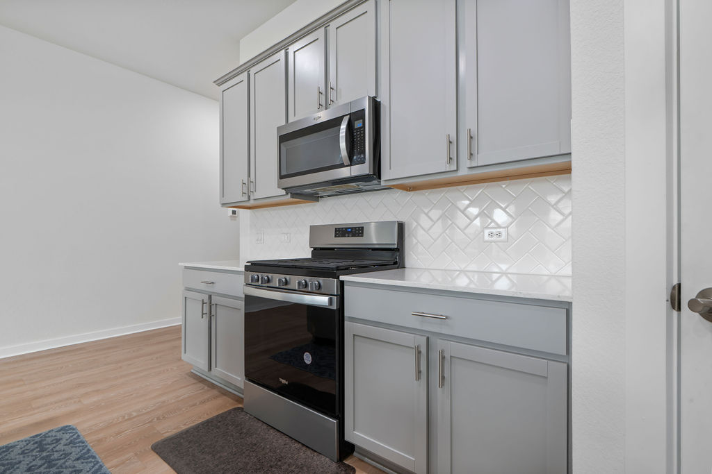 1813 Crow Hop View Leander, TX 78641 - Photo 6 of 33 a kitchen with stainless steel appliances granite countertop white cabinets a microwave oven a sink and dishwasher with wooden floor