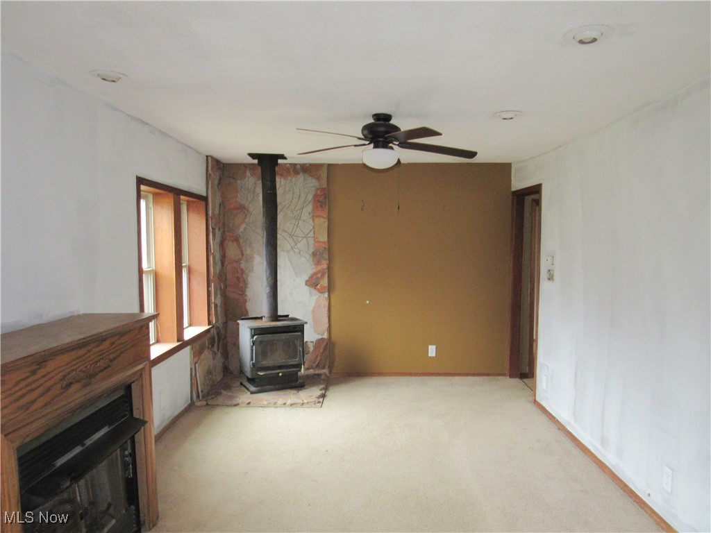 2218 Lake Road Akron, OH 44312 - Photo 4 of 20 Unfurnished living room featuring a wood stove, a ceiling fan, and light colored carpet
