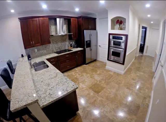 a kitchen with stainless steel appliances kitchen island granite countertop a refrigerator oven a sink with wooden cabinets and floor