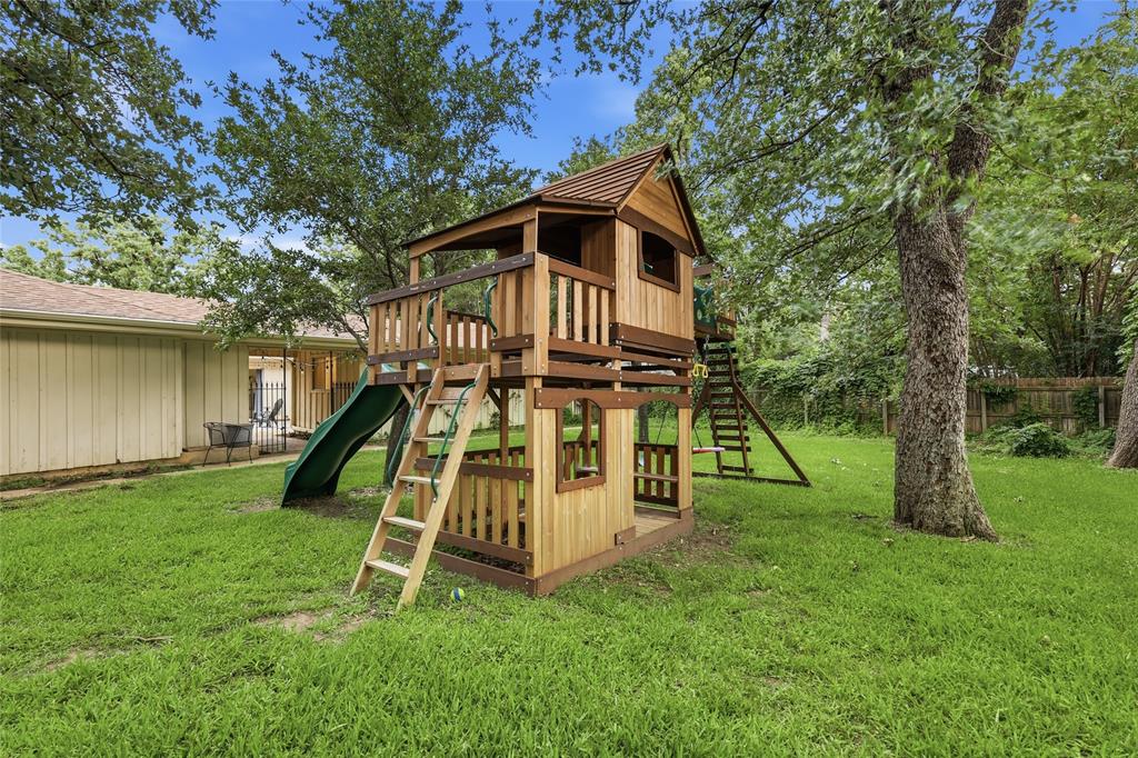823 Ridgecrest Circle Denton, TX 76205 - Photo 37 of 40 Expansive backyard featuring a multi-level wooden play structure with a slide and ladders, mature trees, and a manicured lawn