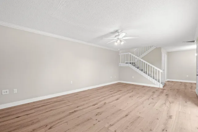 a view of an empty room with wooden floor and a ceiling fan