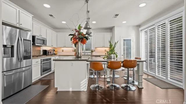 a kitchen with stainless steel appliances kitchen island granite countertop a refrigerator a stove a kitchen island with chairs and wooden floor