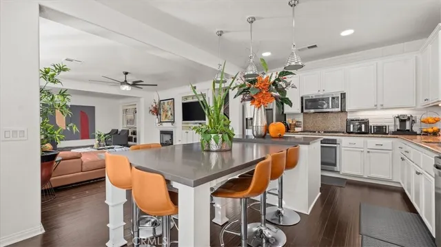 a kitchen with stainless steel appliances granite countertop a stove top oven a refrigerator a kitchen island a dining table and chairs with wooden floor