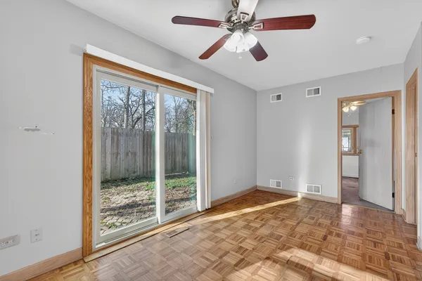 an empty room with chandelier fan and windows