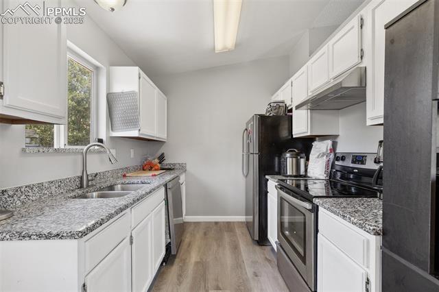 609 Wheat Field Road Fountain, CO 80817 - Photo 12 of 29 Kitchen with appliances with stainless steel finishes, under cabinet range hood, light wood-type flooring, and white cabinets