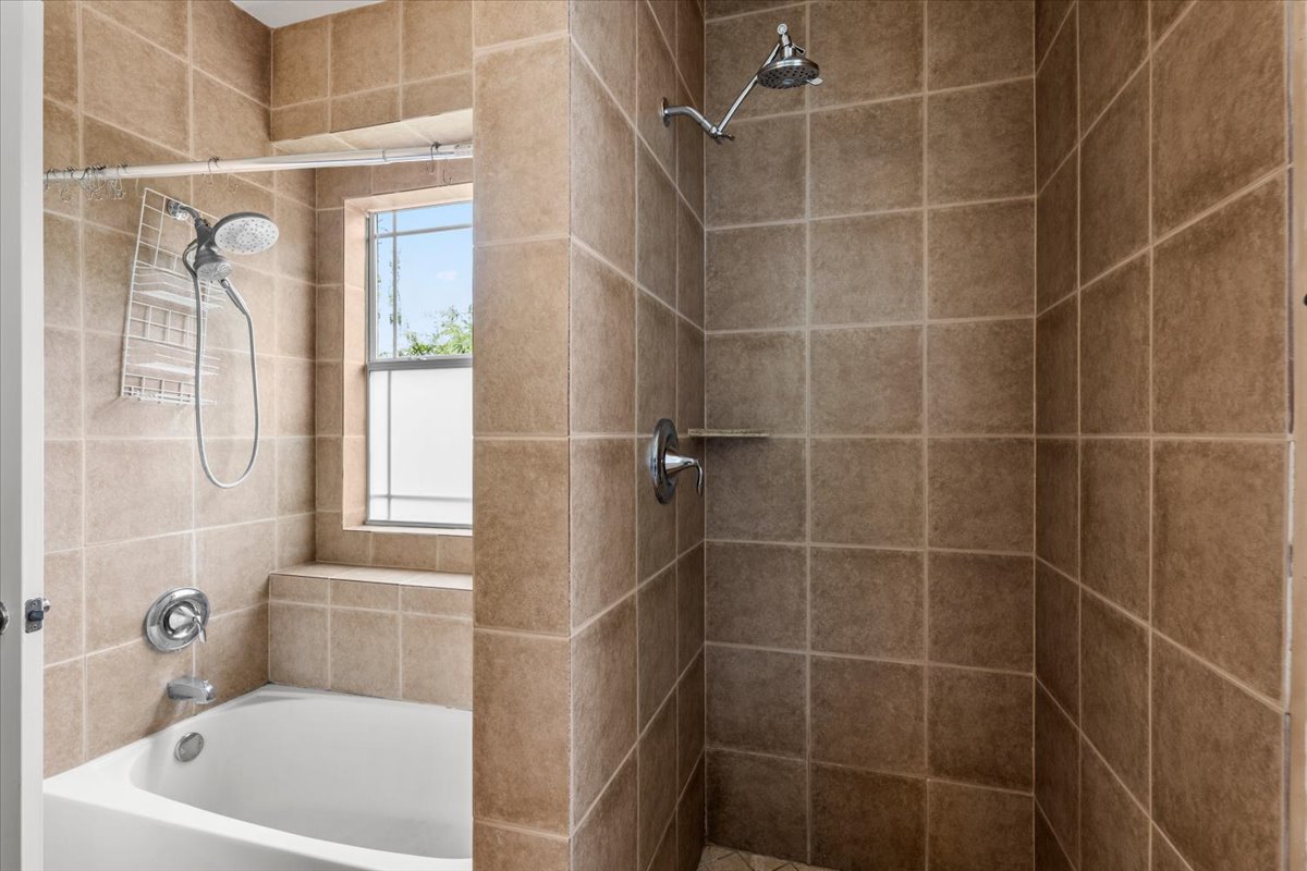 437 Balch Road Elgin, TX 78621 - Photo 15 of 37 A well-lit primary bathroom features a tiled shower and an adjacent tub beneath a window.