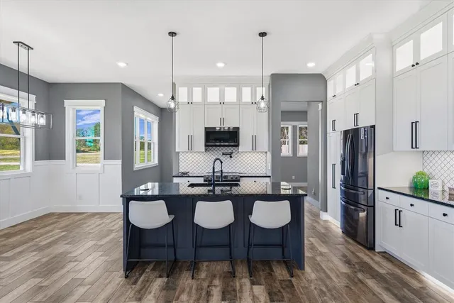 a kitchen with stainless steel appliances granite countertop a refrigerator a sink dishwasher a stove and white cabinets with wooden floor