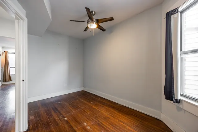 an empty room with wooden floor fan and windows
