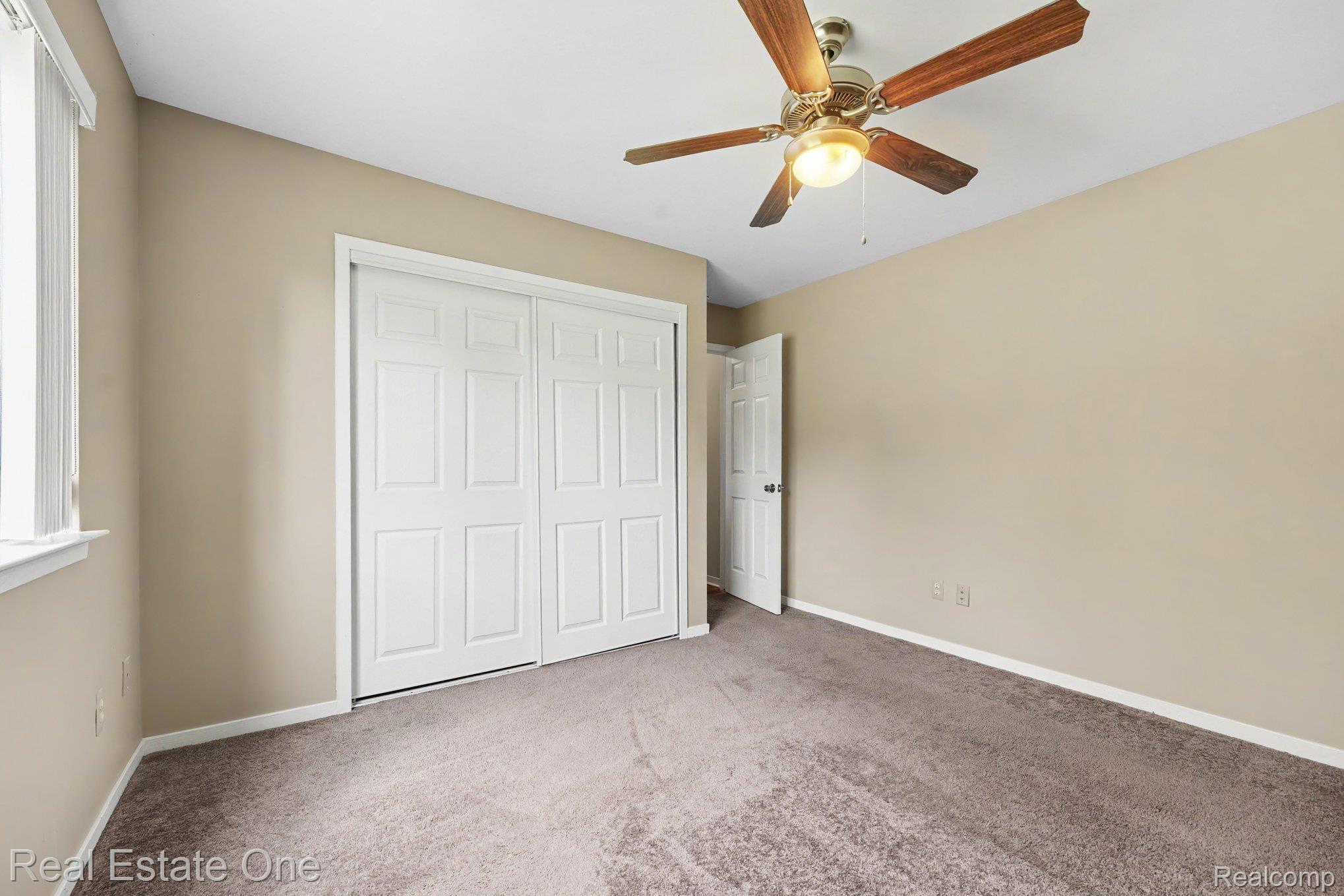 701 Charing Court Rochester, MI 48307 - Photo 16 of 29 Neutral-toned room featuring a wood-finish ceiling fan with integrated lighting, a spacious bi-fold closet, a window with blinds, and soft carpet flooring