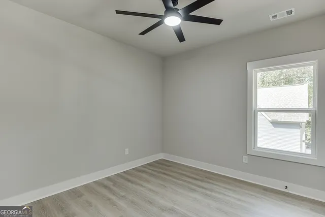 a view of an empty room with wooden floor a ceiling fan and windows