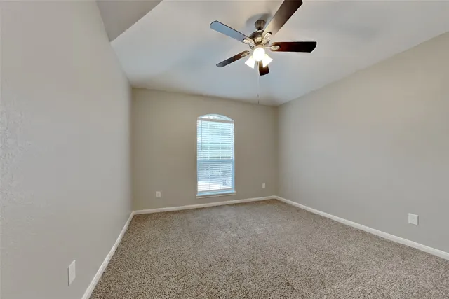 an empty room with chandelier fan and windows
