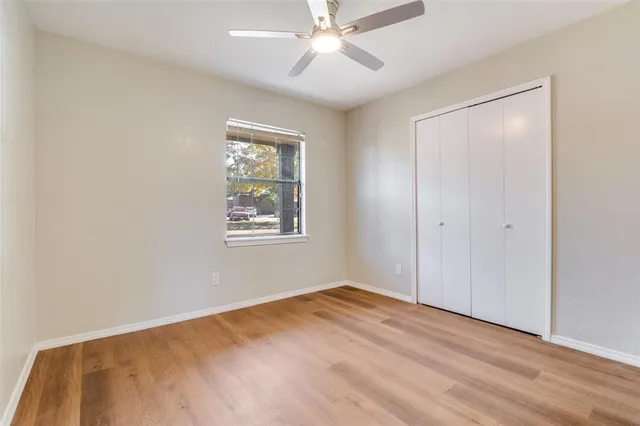 a view of an empty room with wooden floor and a ceiling fan