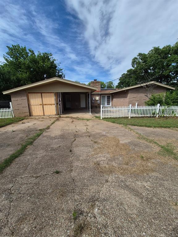 711 Cherry Street Ranger, TX 76470 - Photo 5 of 5 Brick exterior with a covered carport, attached garage, and a white picket fence