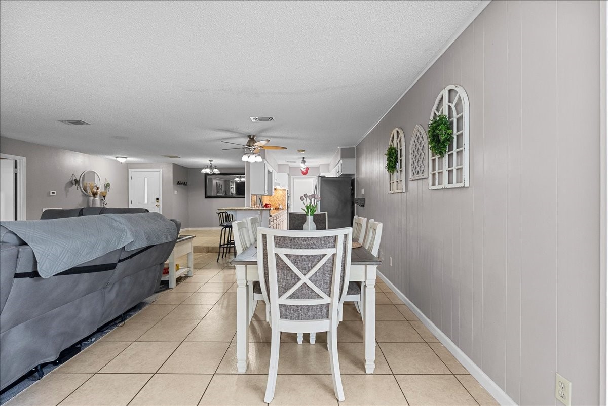 883 Silverpines Road Houston, TX 77062 - Photo 35 of 38 Bright and spacious open-concept living area with neutral tones, tile flooring, and a connected dining space. The room features modern ceiling fans, decorative wall accents, and leads into a kitchen with a breakfast bar.