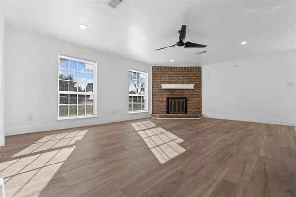 a view of an empty room with wooden floor fireplace and a window