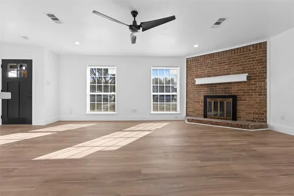 a view of an empty room with wooden floor fireplace and a window