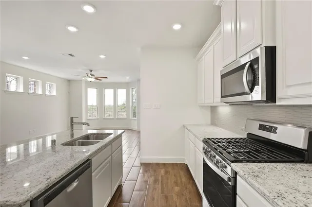 a kitchen with granite countertop stainless steel appliances a sink cabinets and wooden floor