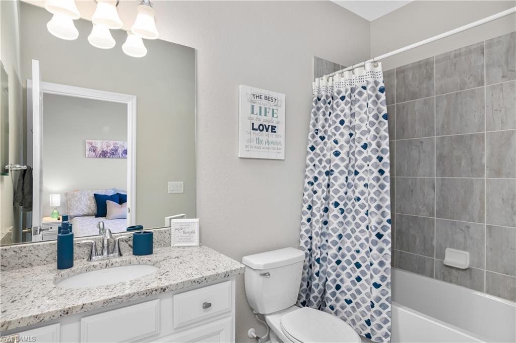 19828 The Pl Boulevard Estero, FL 33928 - Photo 16 of 37 a bathroom with a granite countertop toilet a sink a mirror a shower curtain and a bath tub