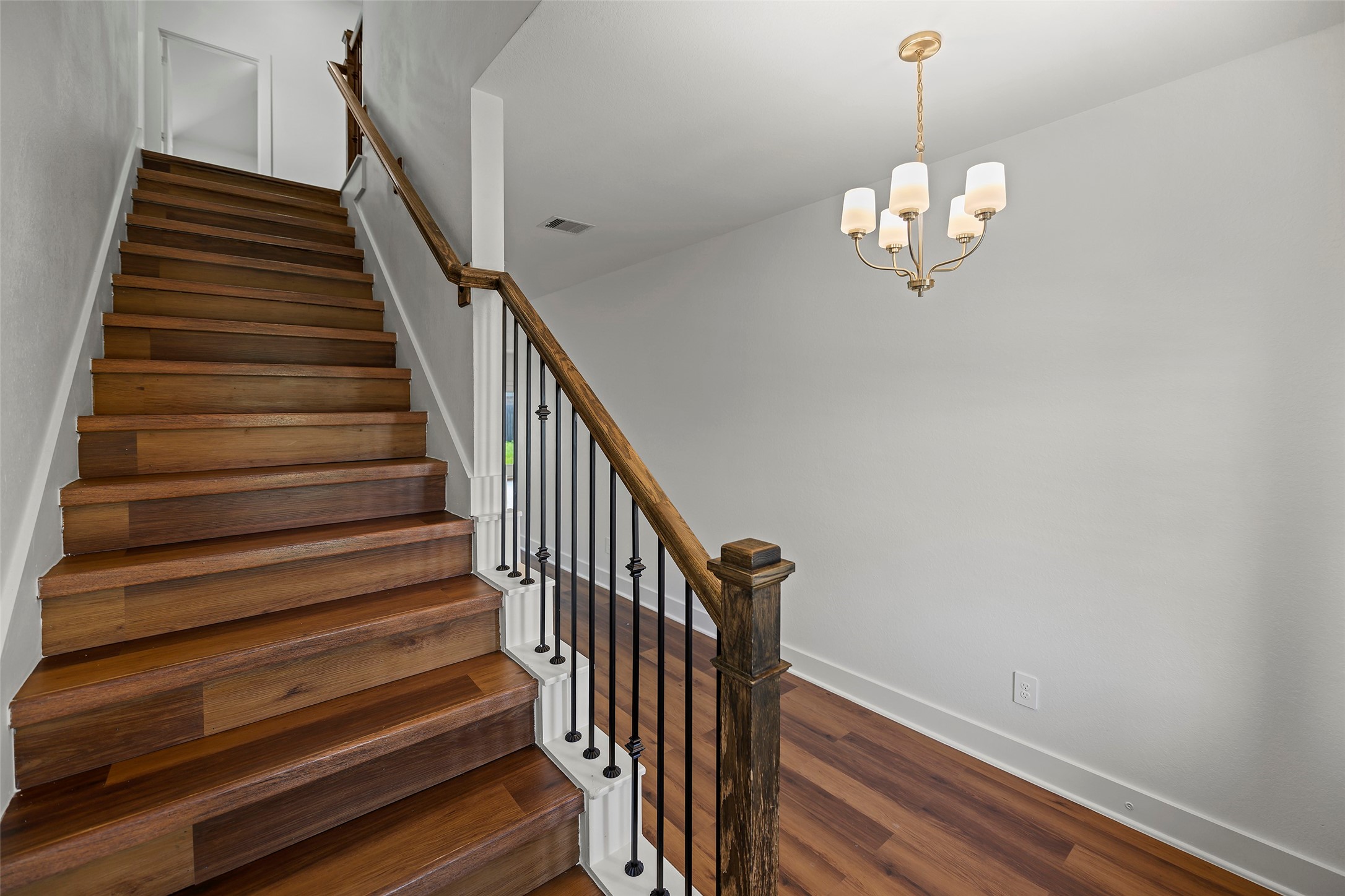 10603 Whitejacket Conroe, TX 77385 - Photo 6 of 42 This photo showcases a bright entryway with a wooden staircase and elegant iron balusters. The space is complemented by a modern chandelier, creating a welcoming and stylish atmosphere.