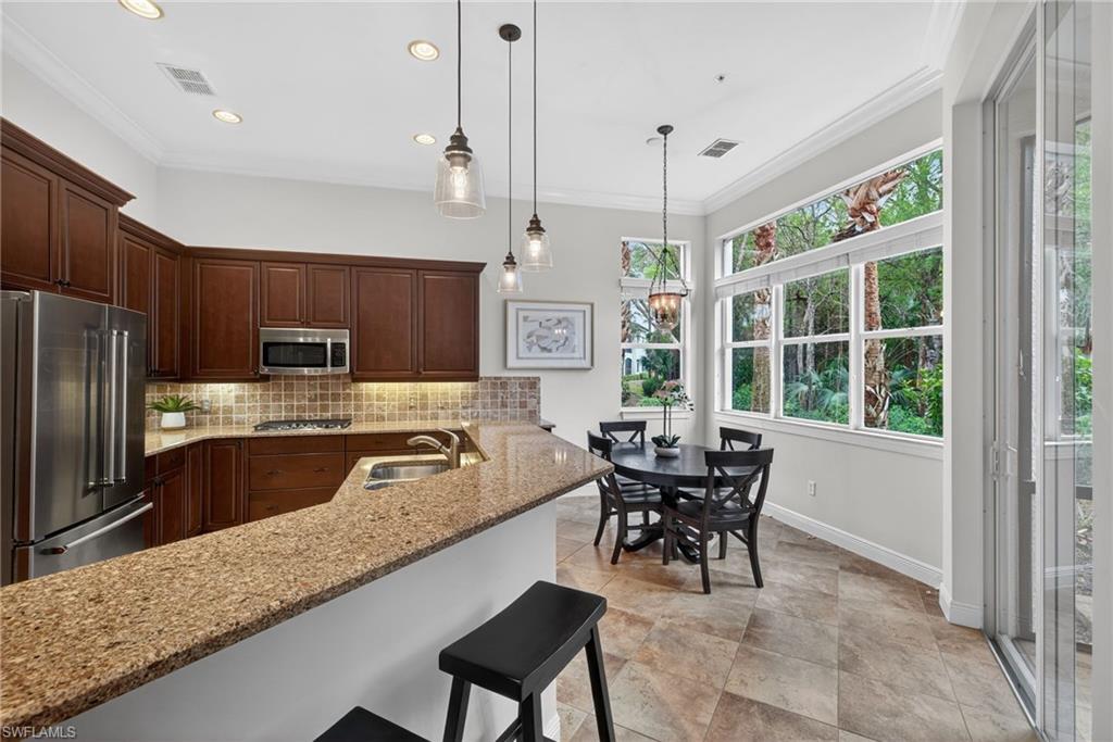 28540 Calabria Court, Unit 101 Naples, FL 34110 - Photo 8 of 41 Kitchen featuring stainless steel appliances, light stone countertops, ornamental molding, a breakfast bar area, and pendant lighting