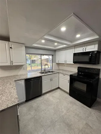 a large white kitchen with granite countertop a stove top oven a sink dishwasher and a refrigerator with wooden cabinets