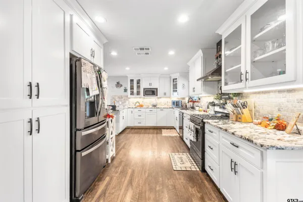 a kitchen with stainless steel appliances kitchen island granite countertop a refrigerator a sink dishwasher a stove and white cabinets with wooden floor